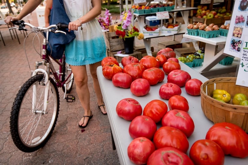 Girl with bike at the farmers market looking at tomatoes